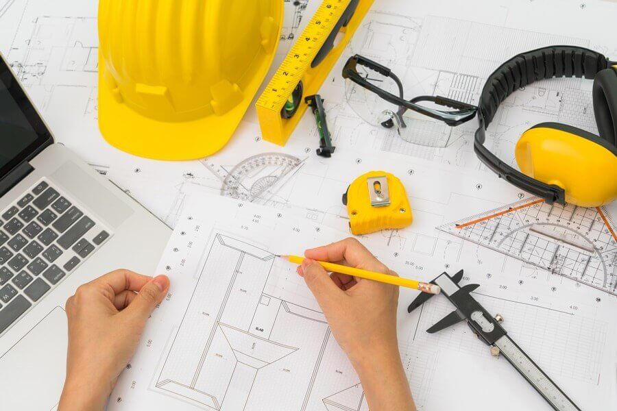 Hand over Construction plans with yellow helmet and drawing tools on blueprints
