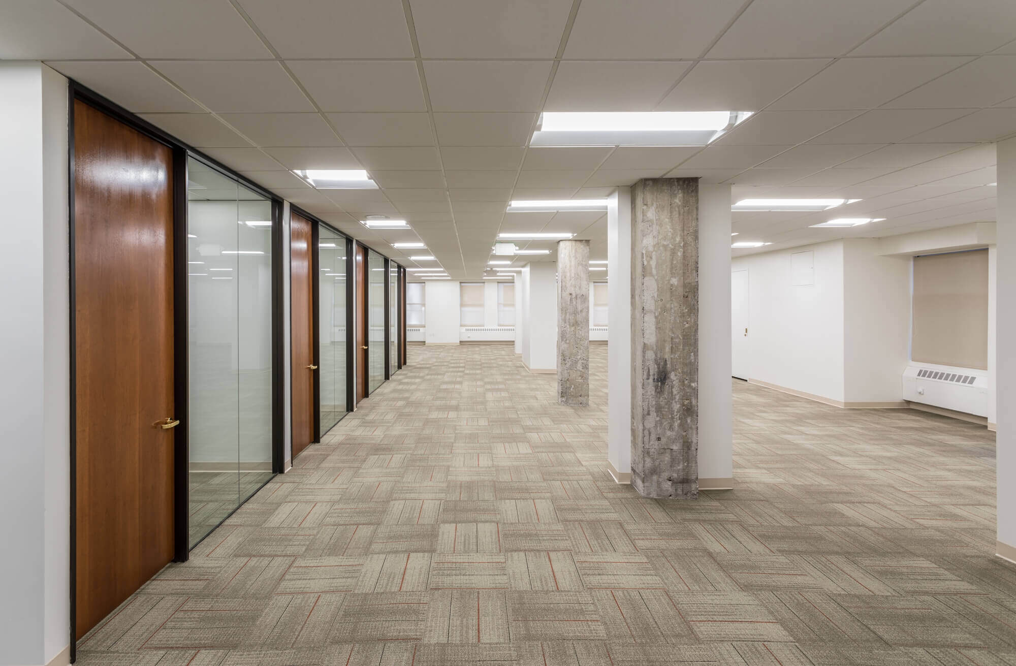 a large room with concrete pillars, glass area, white ceiling and wooden flooring