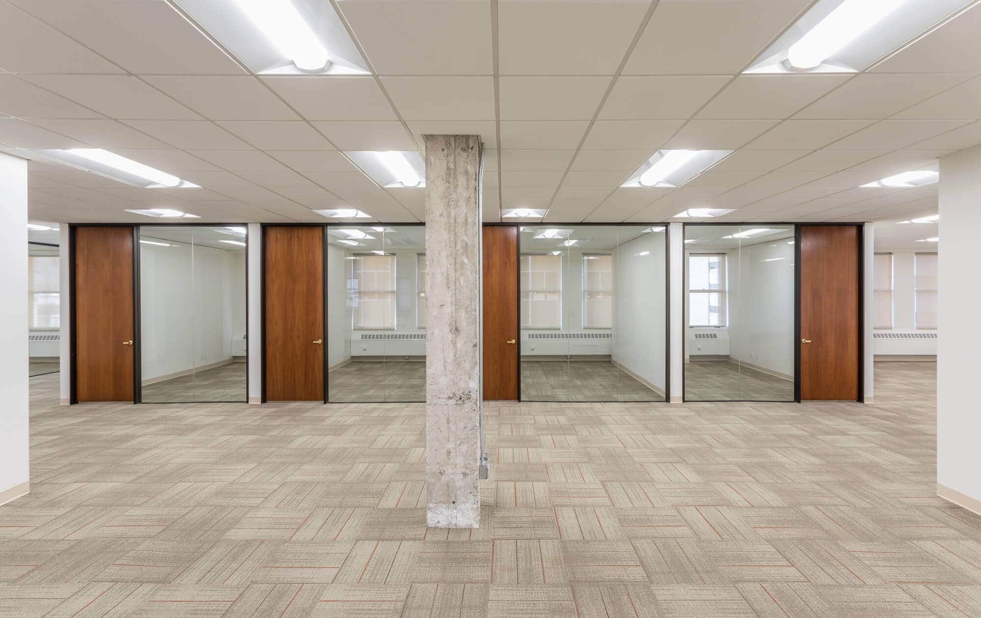 a large room with concrete pillars, glass area and wooden flooring