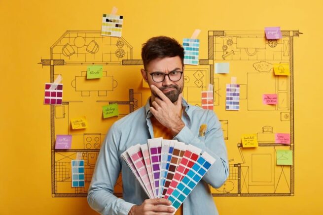 Interior construction contractor poses with color swatches, stands against model of interior architecture.
