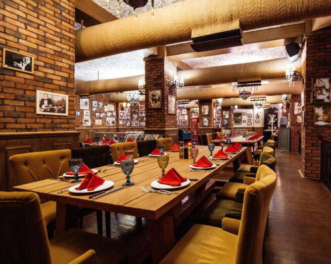 A restaurant hall with construction of red brick walls wooden tables and pipes in the ceiling