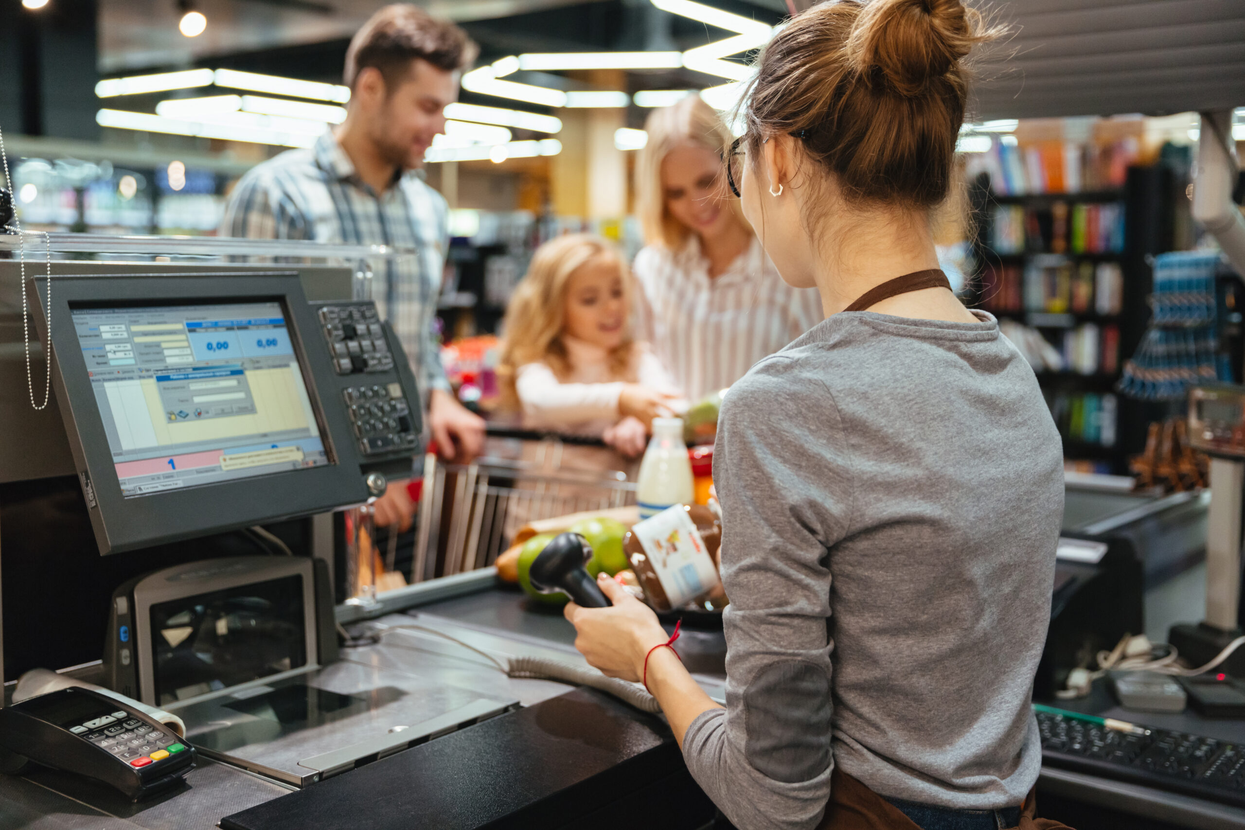 A family standing at the cash counter buying groceries at the supermarket retail store.